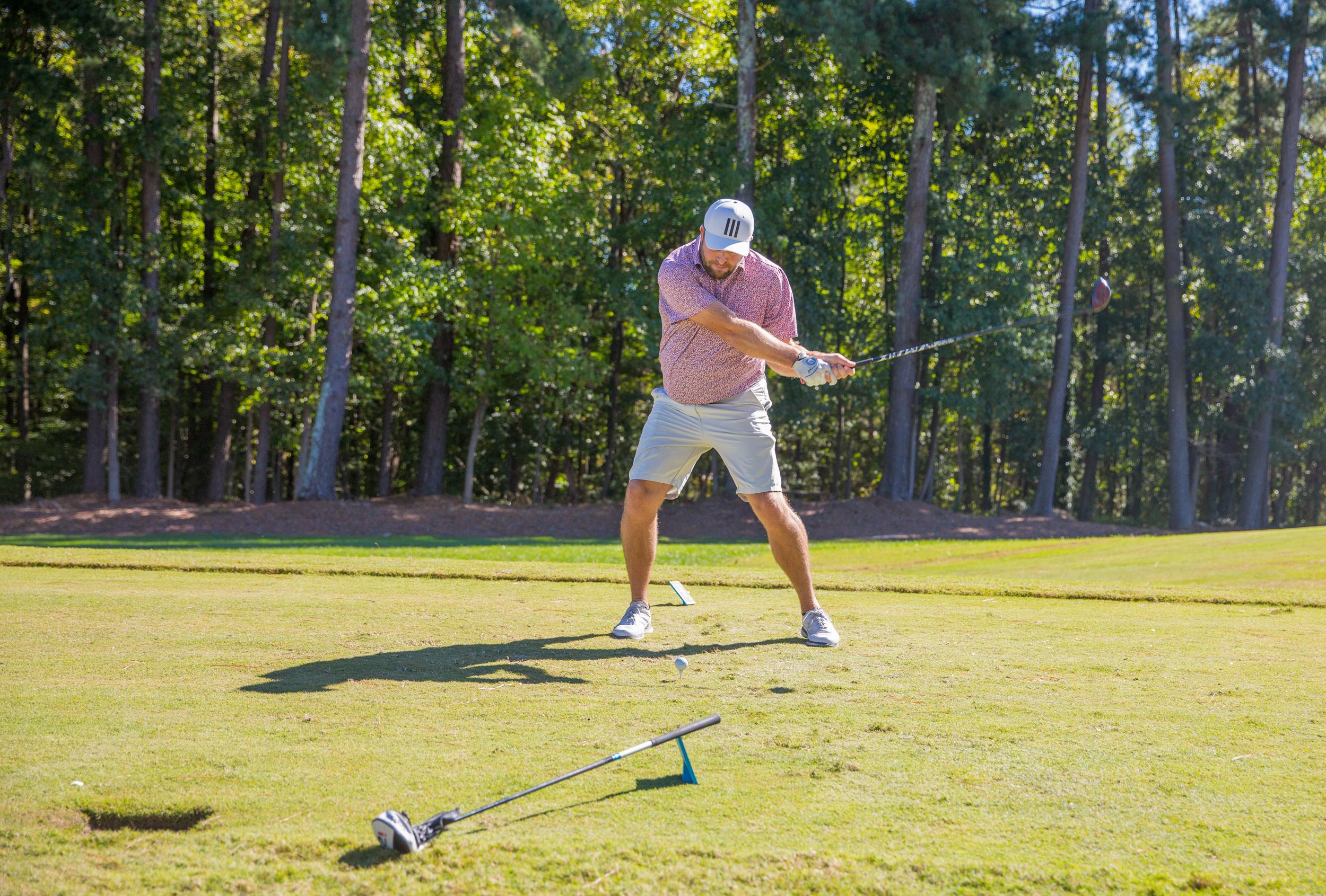 A man mid-swing on a golf course, surrounded by trees and sunlight.