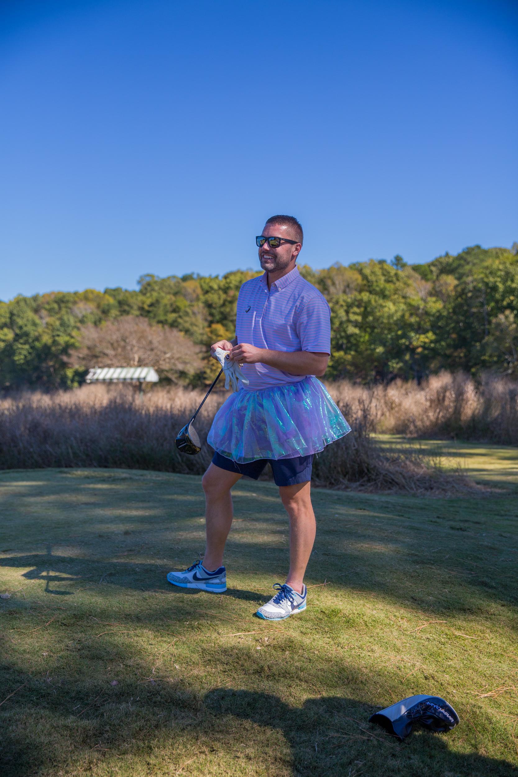 Person in a tutu holding a golf club on a sunny golf course.