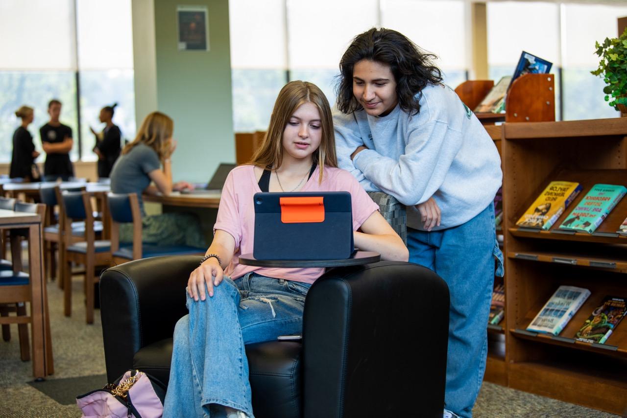 Two students in the library, using an iPad to study and research.