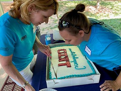 Two women in blue T-shirts look at a cake that says "Congratulations TRIO."