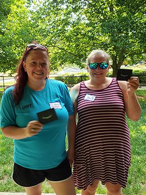 Two women standing outdoors holding Amazon gift cards, with trees in the background.