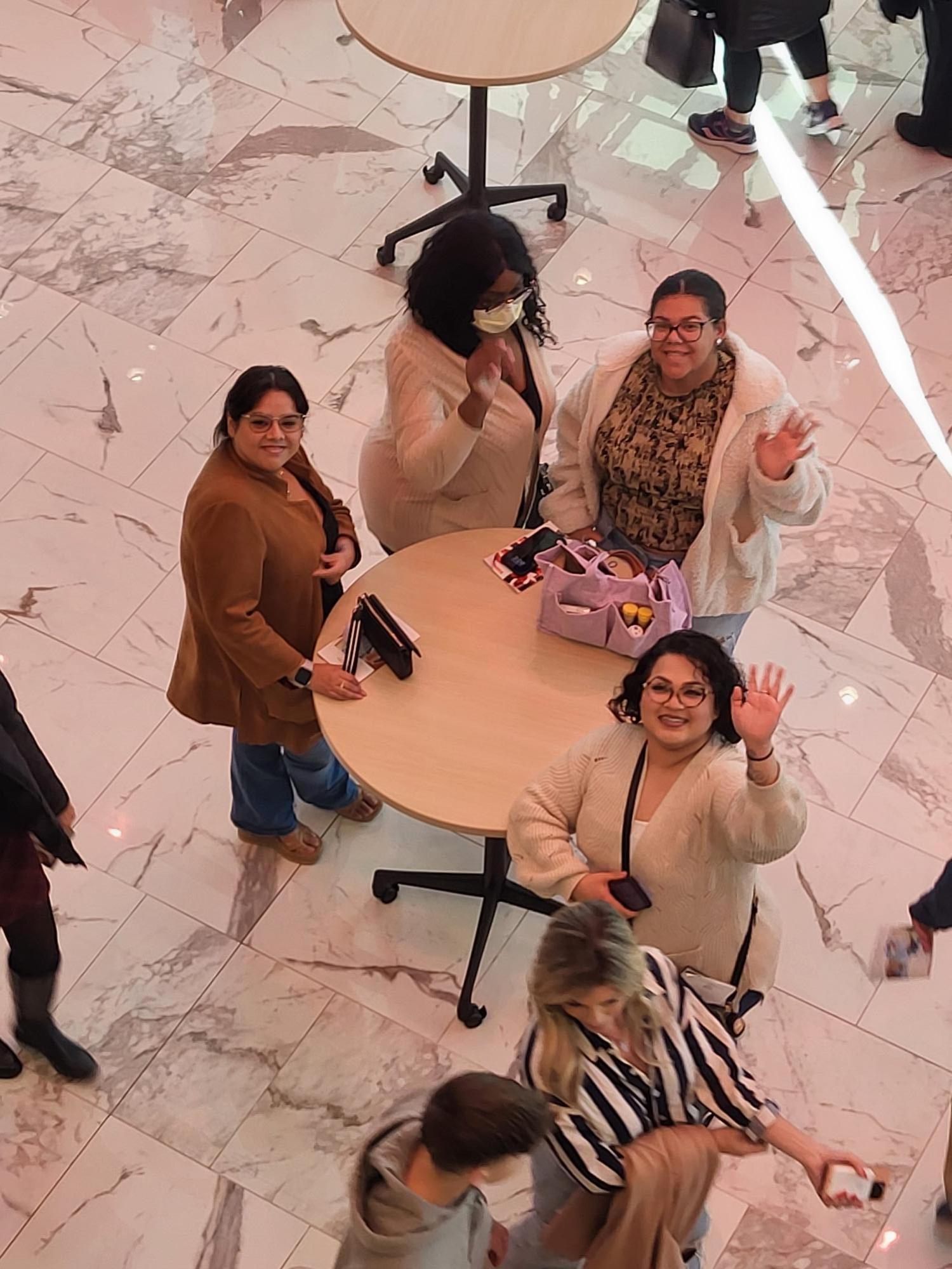 People waving and looking up in a marbled-floor room with tables.